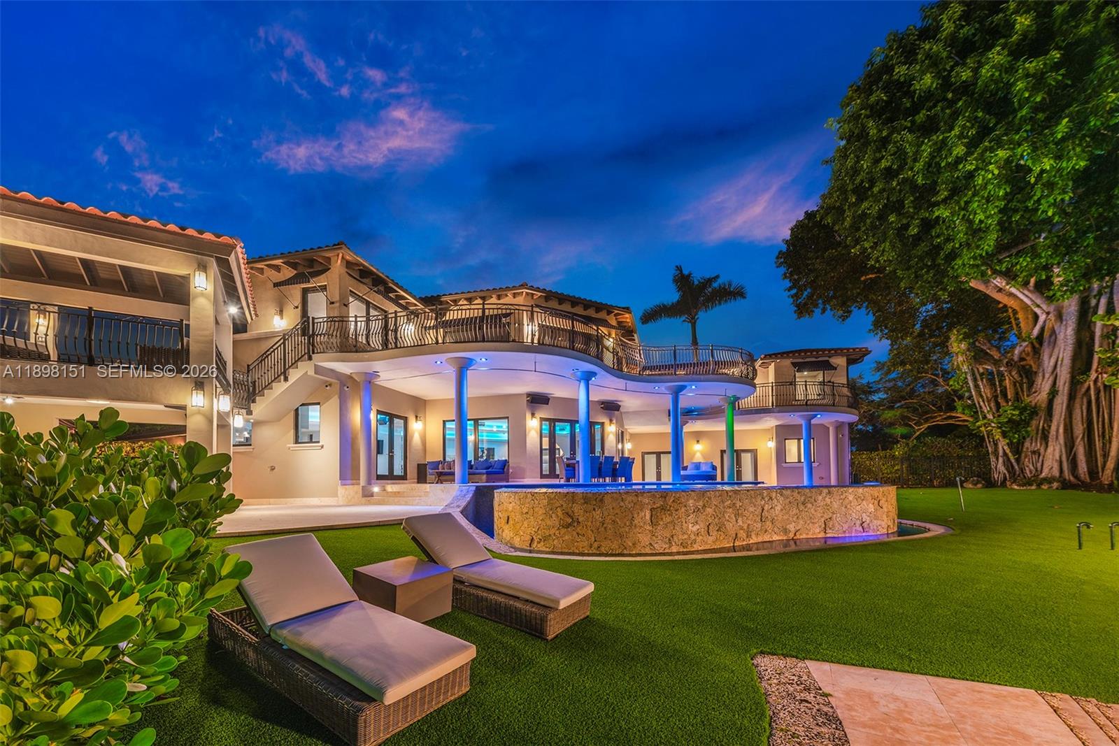 A two-story house features a curved balcony, a stone-walled pool, and lounge chairs on grass — 6700 Granada Blvd, Coral Gables FL 33146, CORAL GABLES, FL