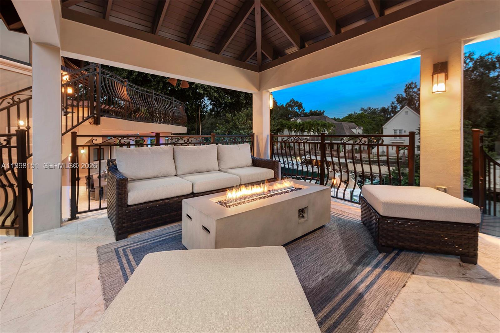 A covered outdoor patio features a wicker sofa, a fire pit table, and metal railings — 6700 Granada Blvd, Coral Gables FL 33146, CORAL GABLES, FL