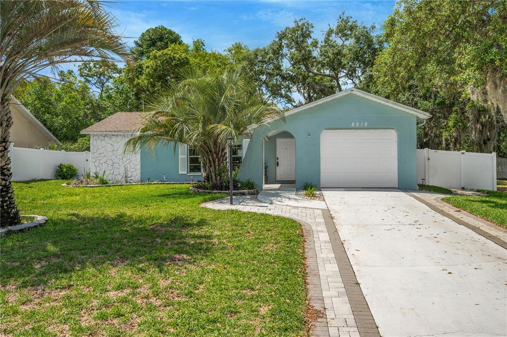 A single-story house with light blue stucco, a white garage door, and a paved walkway — 8218 PLACID STREET, SPRING HILL, FL