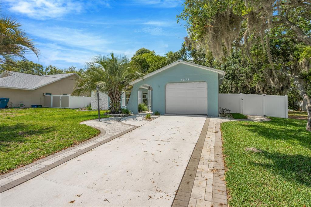 A light blue single-story house features a white garage door and a paved driveway — 8218 PLACID STREET, SPRING HILL, FL