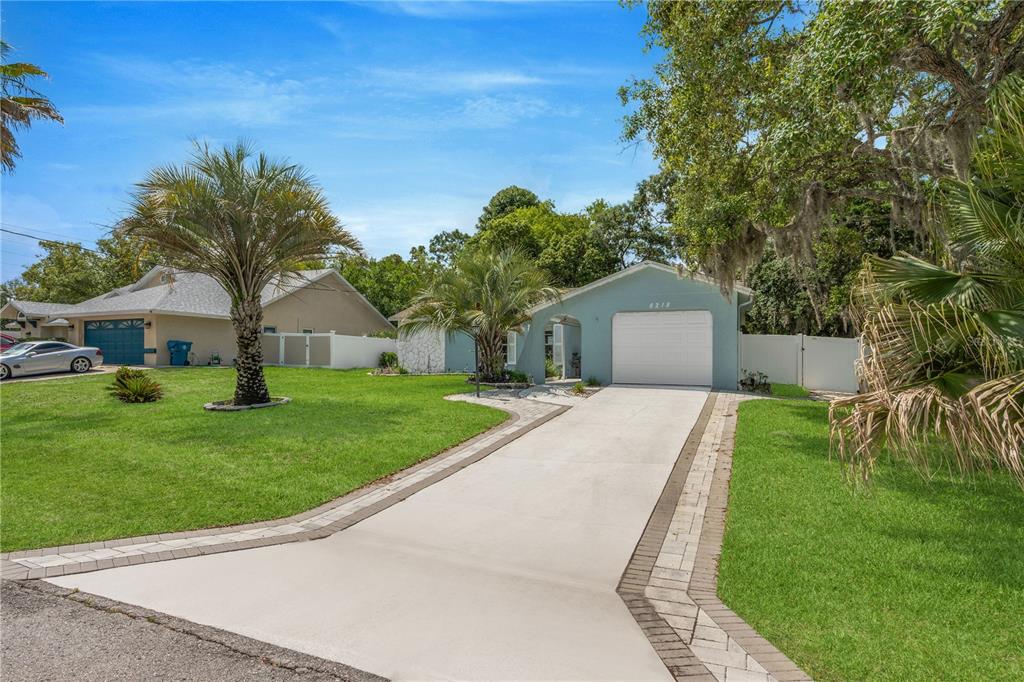 A light blue house with a white garage door and a paved driveway sits on grass — 8218 PLACID STREET, SPRING HILL, FL