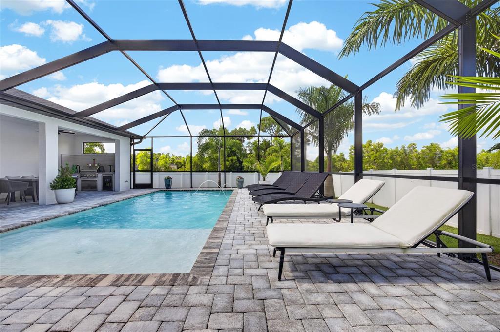 A swimming pool with a screened enclosure, lounge chairs, and a covered outdoor kitchen area — 4700 NW 38TH AVENUE, CAPE CORAL, FL