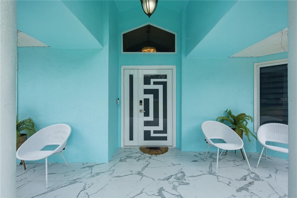 A bright turquoise covered entryway features white modern chairs and a patterned double front door — 16839 WHIRLEY ROAD, LUTZ, FL