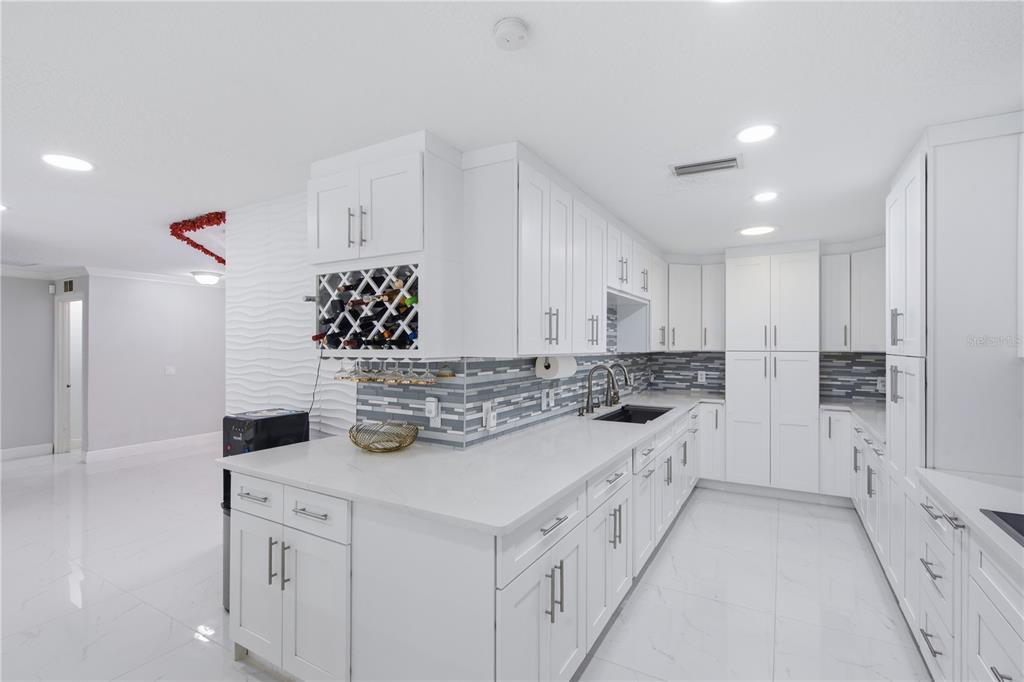 A modern white kitchen features quartz countertops, a tiled backsplash, and a built-in wine rack — 16839 WHIRLEY ROAD, LUTZ, FL