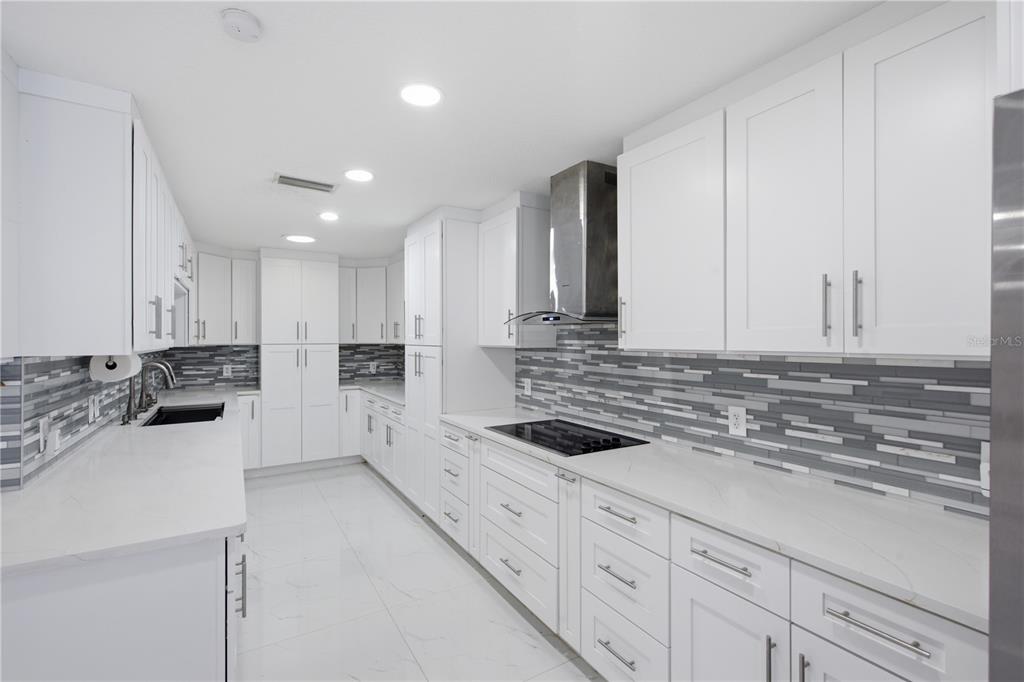 A modern kitchen features white cabinets, marble-style countertops, and a gray-toned horizontal tile backsplash — 16839 WHIRLEY ROAD, LUTZ, FL