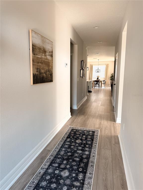 A hallway with light wood-look flooring leads to an open dining area with a rug — 12827 SW 61ST AVENUE, OCALA, FL