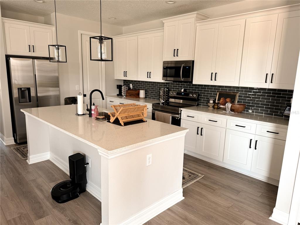 A modern kitchen features white cabinetry, stainless steel appliances, a quartz island, and dark backsplash — 12827 SW 61ST AVENUE, OCALA, FL