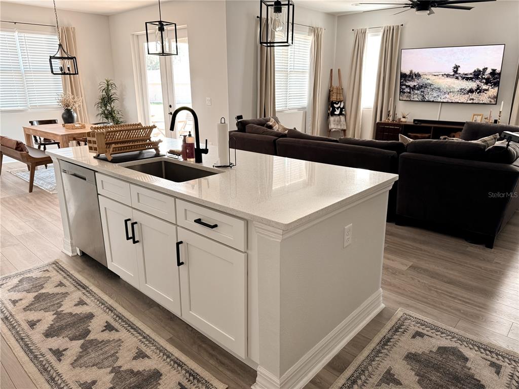 A kitchen island with white cabinets and a quartz countertop sits before a living area — 12827 SW 61ST AVENUE, OCALA, FL