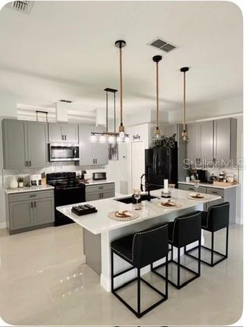 A modern kitchen features gray cabinets, a white quartz island, and three hanging pendant lights — 14 WAYLAND PLACE, PALM COAST, FL