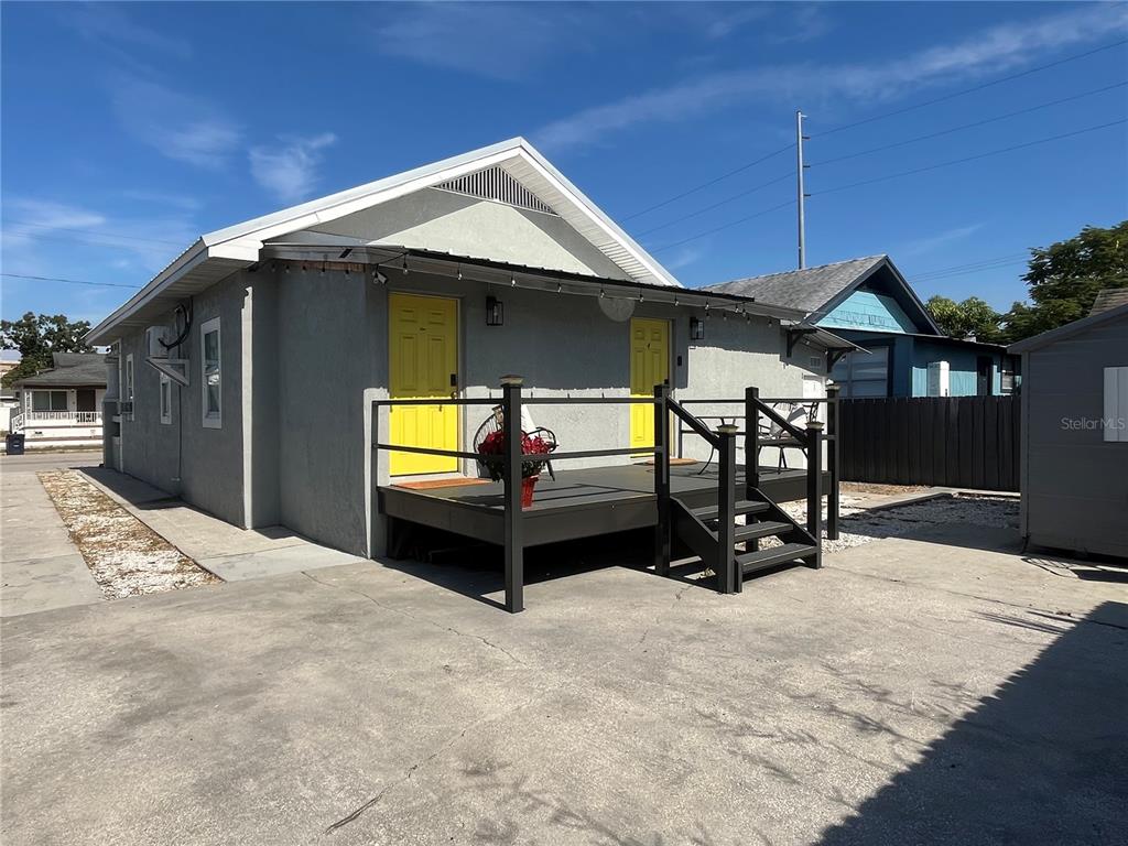 A gray house with two yellow doors and a dark wooden deck sits on a concrete lot — 2510 W MAIN STREET, TAMPA, FL