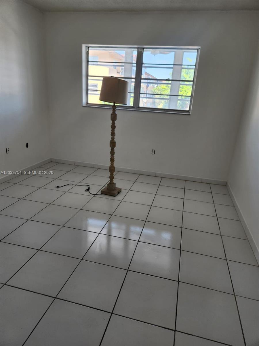 An empty room features white tiled floors, plain white walls, and a single floor lamp — 160 Royal Palm Rd # 215, Hialeah Gardens FL 33016, HIALEAH GARDENS, FL