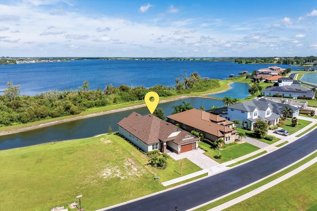 An aerial view shows a single-family house with a brown roof beside a lake — 559 WATERFERN TRAIL DRIVE, AUBURNDALE, FL