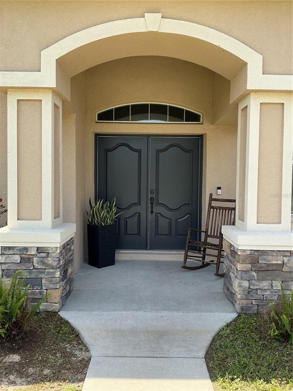 A covered front porch features double doors, stone-based columns, and a wooden rocking chair — 13262 CROWELL ROAD, BROOKSVILLE, FL