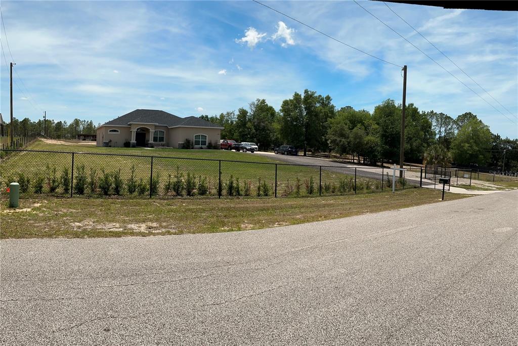 A single-story house with a fenced yard sits behind a paved road under a blue sky — 13262 CROWELL ROAD, BROOKSVILLE, FL
