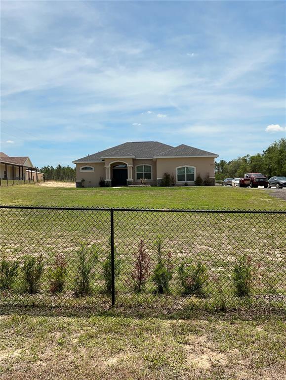 A single-story house with a tan stucco exterior sits behind a chain-link fence — 13262 CROWELL ROAD, BROOKSVILLE, FL