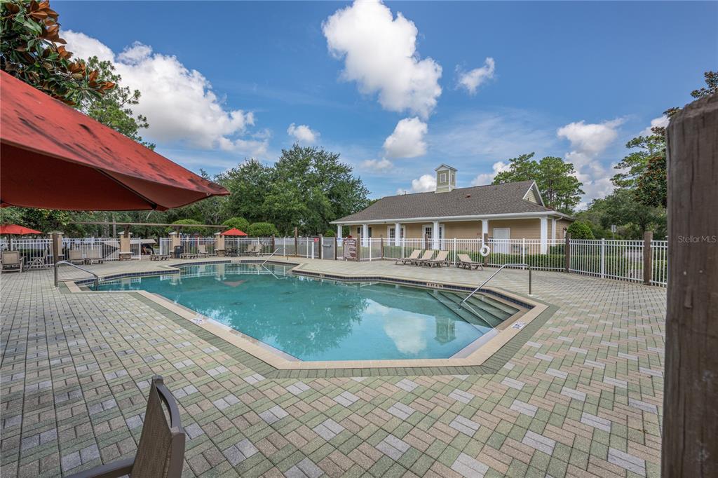 A swimming pool with a paved deck and a clubhouse building under a blue sky — 930 MOONLIGHT COVE ROAD UNIT 11-107, ORANGE CITY, FL