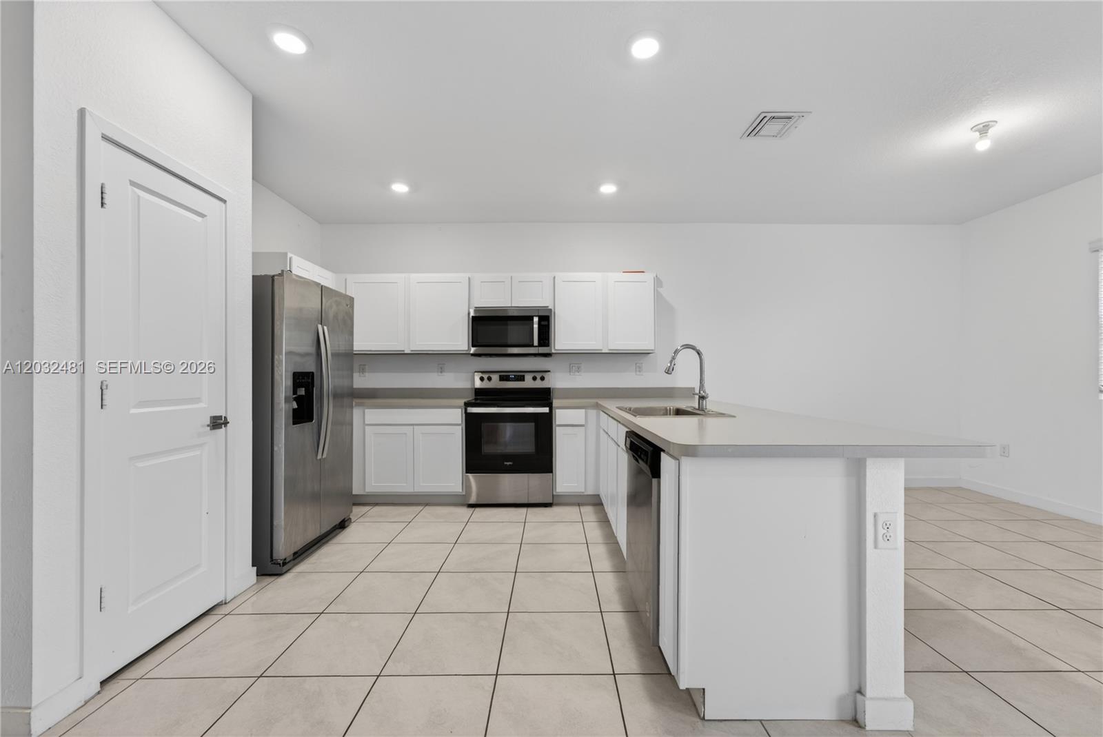 A kitchen features white cabinets, stainless steel appliances, a peninsula, and light-colored tile flooring — 1780 SE 9th Ave, Homestead FL 33034, HOMESTEAD, FL