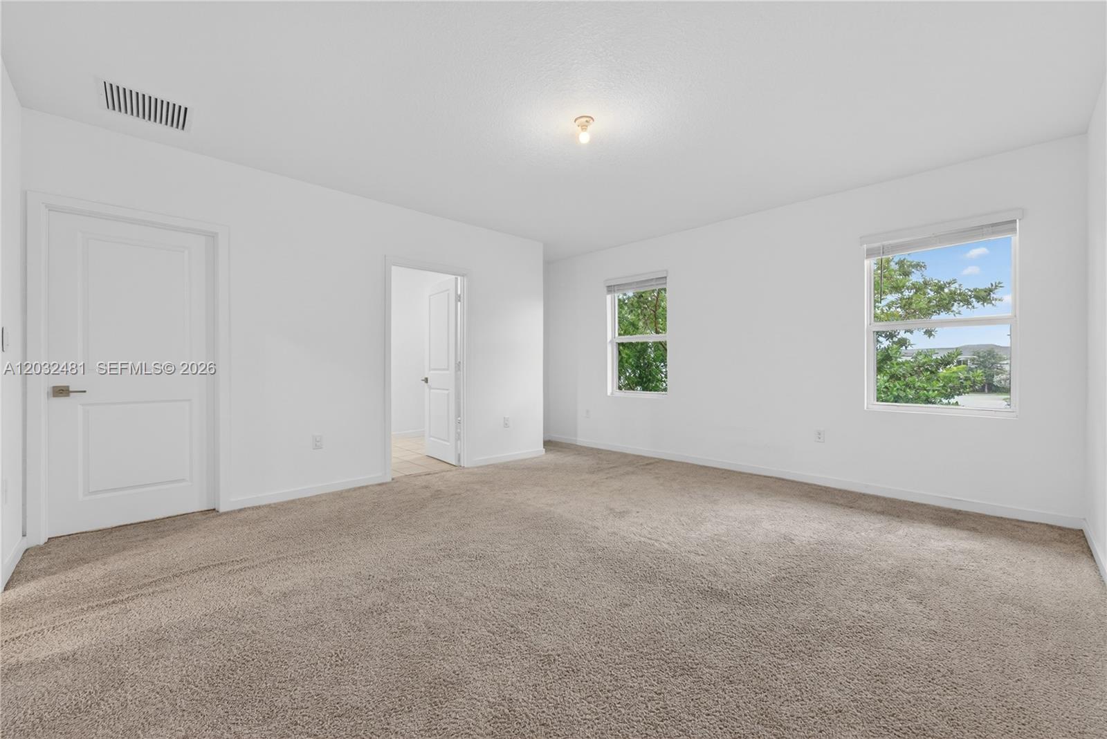 An empty bedroom features beige carpeting, white walls, two windows, and two interior doors — 1780 SE 9th Ave, Homestead FL 33034, HOMESTEAD, FL