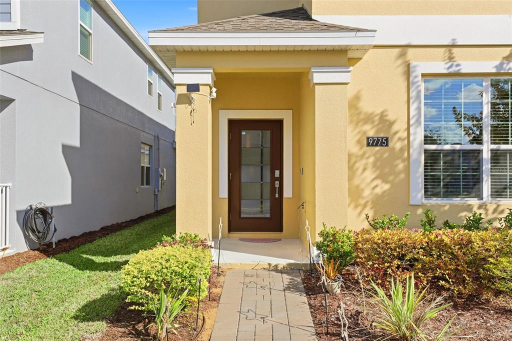 The exterior view shows a yellow house entrance with a brown front door and walkway — 9775 INTRODUCTION WAY, ORLANDO, FL