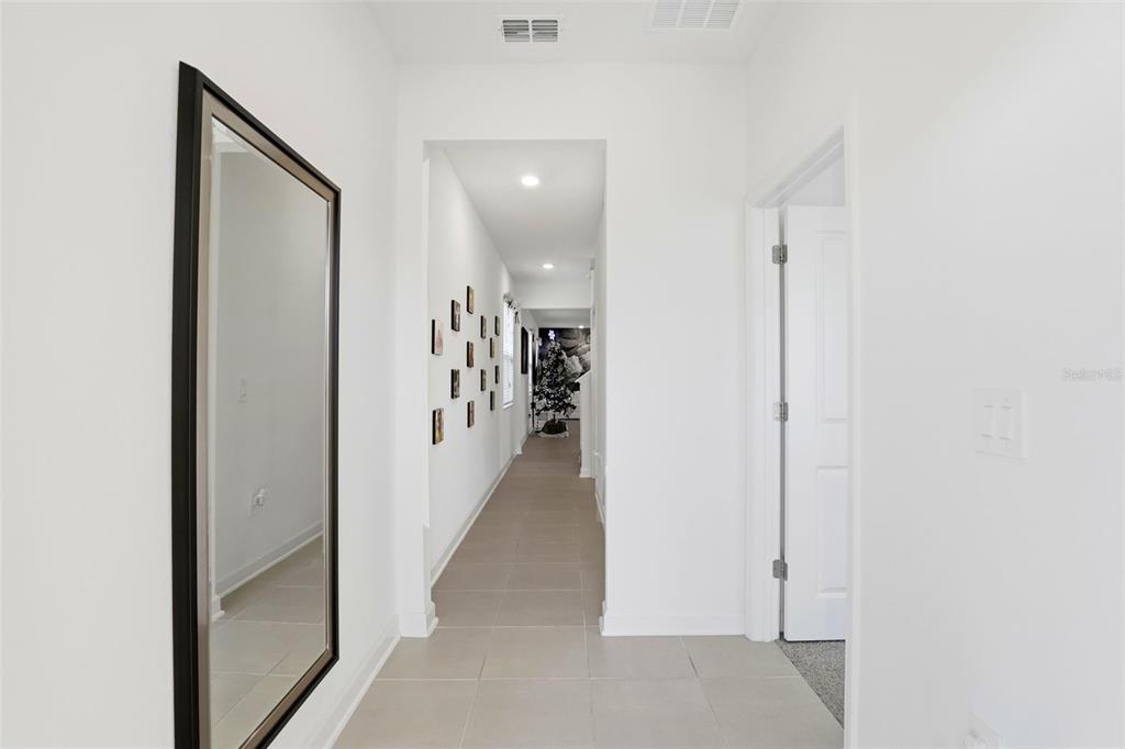 A hallway with light tile flooring, a large wall mirror, and a gallery wall — 9775 INTRODUCTION WAY, ORLANDO, FL