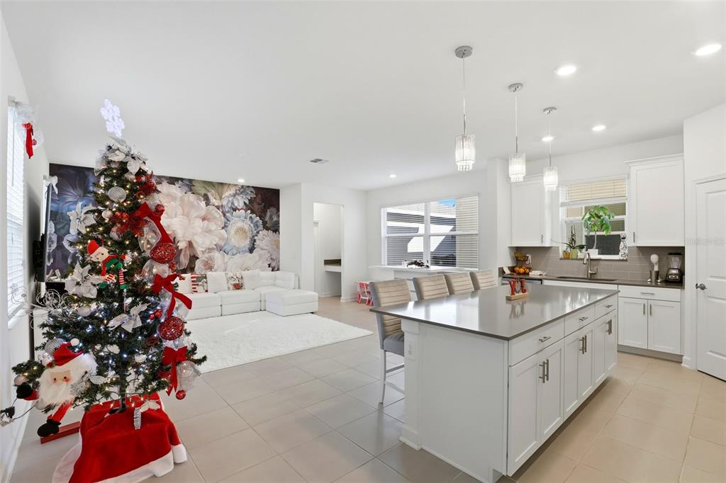 A bright open-concept kitchen and living area featuring a Christmas tree and floral accent wall — 9775 INTRODUCTION WAY, ORLANDO, FL