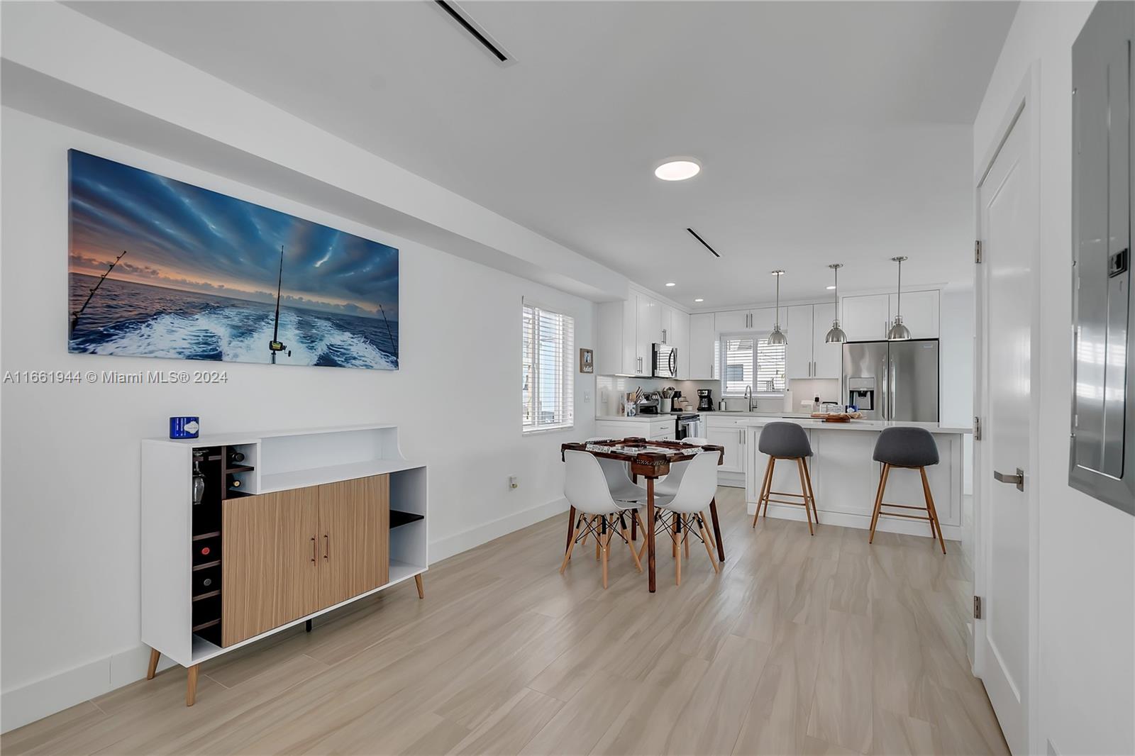 This open-concept kitchen and dining area features white cabinetry, light wood-look flooring, and bar seating — 94825 Overseas Highway # 144, Key Largo FL 33037, KEY LARGO, FL