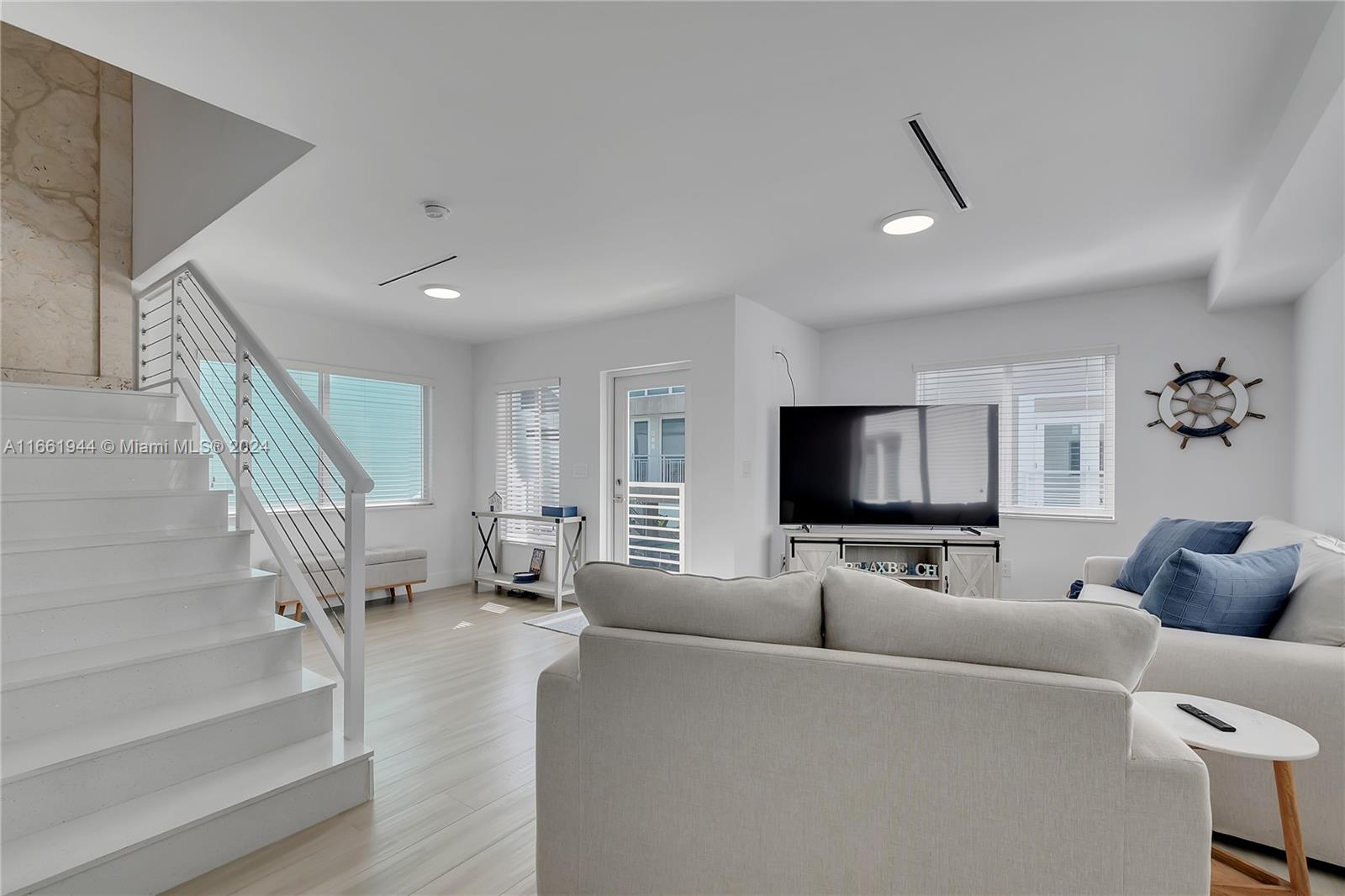 A bright living room features white walls, light wood flooring, a staircase, and a television — 94825 Overseas Highway # 144, Key Largo FL 33037, KEY LARGO, FL