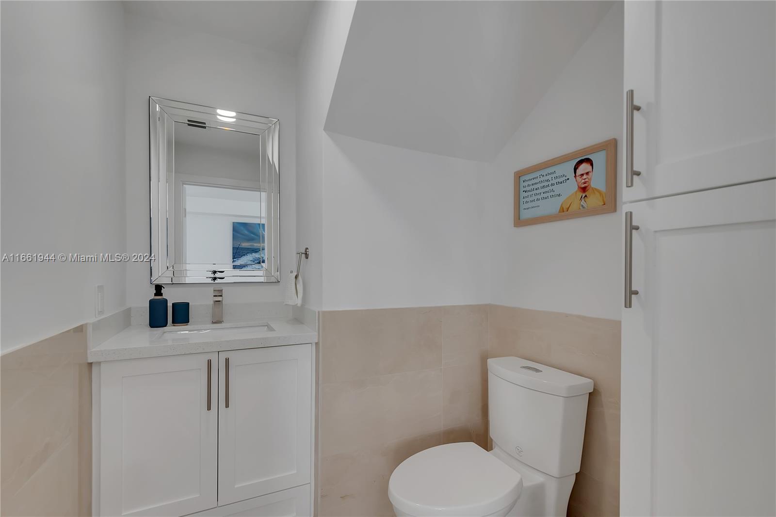 A small bathroom features a white vanity, a mirror, a toilet, and wall-mounted artwork — 94825 Overseas Highway # 144, Key Largo FL 33037, KEY LARGO, FL