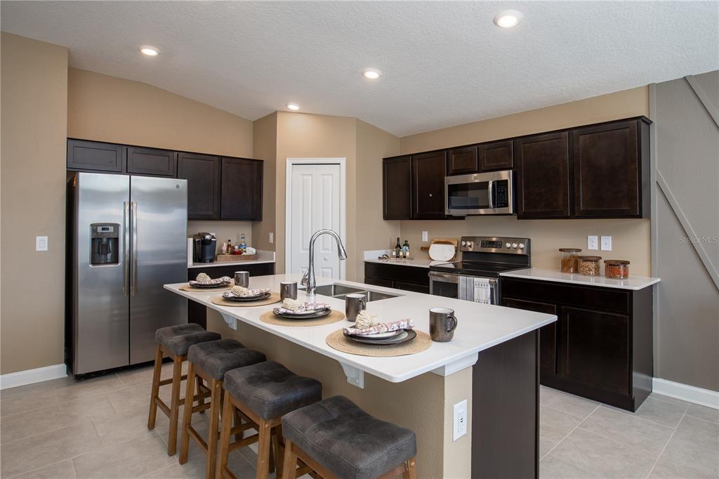 A kitchen features dark wood cabinets, stainless steel appliances, a white island, and bar stools — 5228 WORCHESTER DRIVE, KISSIMMEE, FL