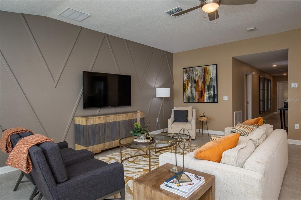 A living room features a geometric accent wall, a television, and neutral-toned furniture — 5228 WORCHESTER DRIVE, KISSIMMEE, FL