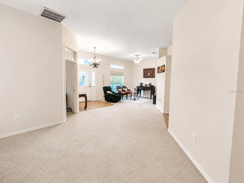 A spacious living area features beige carpeting, a chandelier, and a view of the entryway — 5635 CANVASBACK COURT, LAKELAND, FL