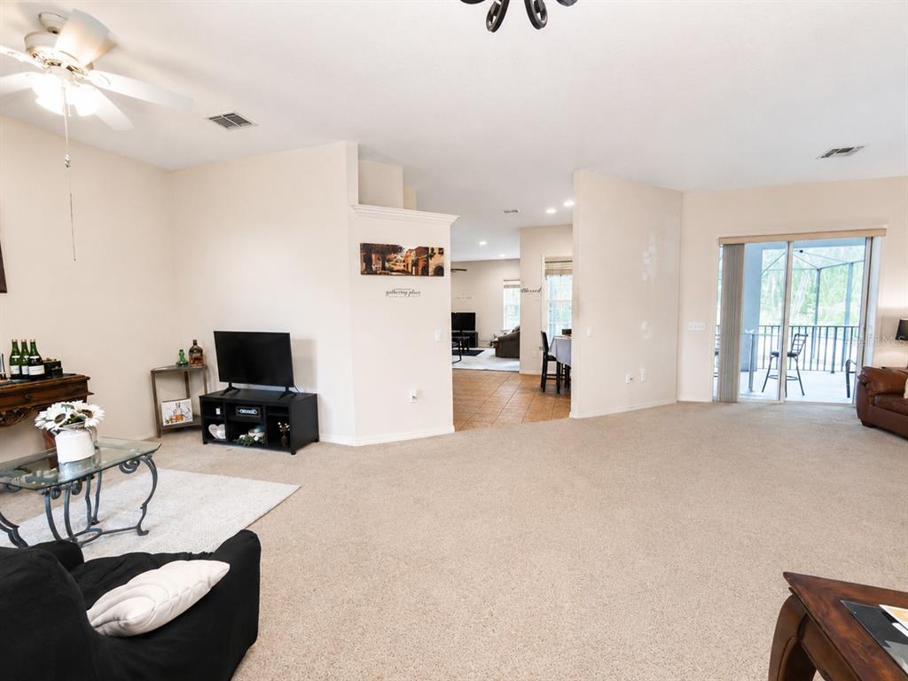 A spacious living room with beige carpet, a ceiling fan, and a view into another room — 5635 CANVASBACK COURT, LAKELAND, FL