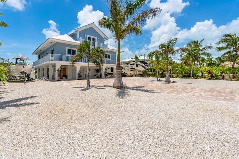 A light blue stilt house with a gravel driveway, a boat, and a parked RV — KEY LARGO, FL