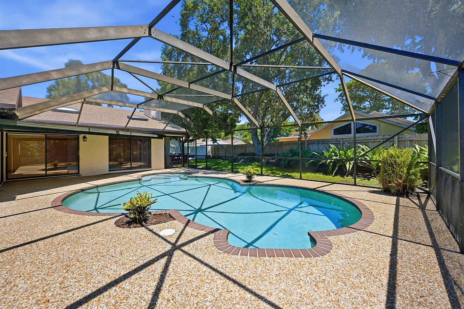 A swimming pool with a brick border sits inside a screened-in patio enclosure — 21540 Kapok Circle, Boca Raton FL 33433, BOCA RATON, FL