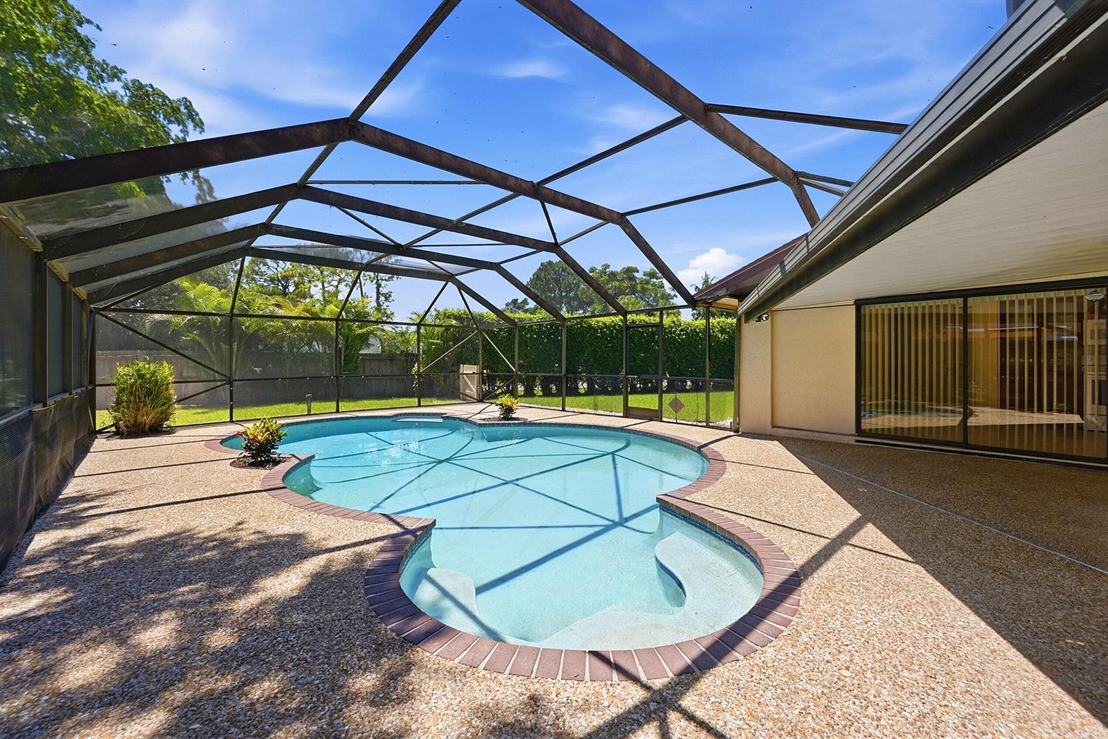 A screened-in patio features a kidney-shaped swimming pool with a brick-trimmed edge — 21540 Kapok Circle, Boca Raton FL 33433, BOCA RATON, FL