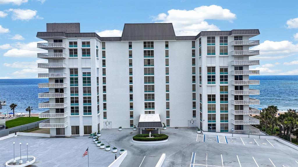 An exterior view of a white multi-story beachfront condominium building with balconies and a parking lot — 1575 OCEAN SHORE BOULEVARD UNIT 805, ORMOND BEACH, FL