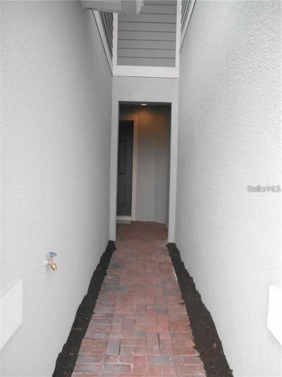 A narrow outdoor walkway with red brick pavers leads to a dark front door — 6344 CAMINO DRIVE, APOLLO BEACH, FL