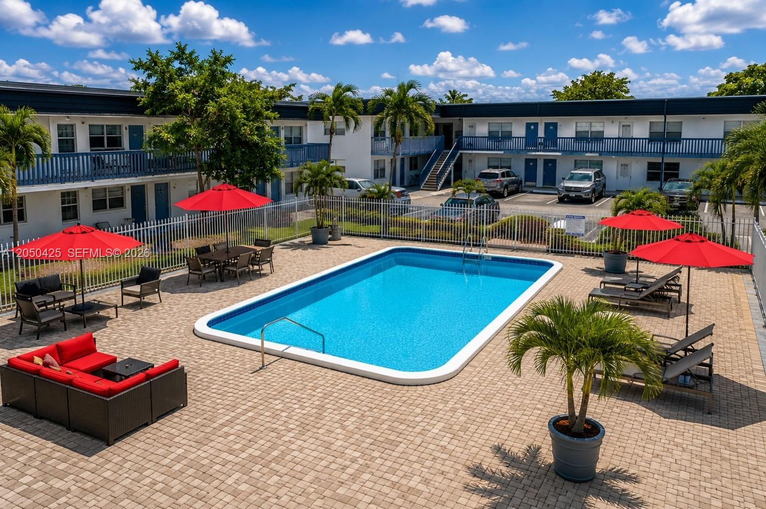 An outdoor swimming pool area with lounge chairs, red umbrellas, and a residential building — MIRAMAR, FL