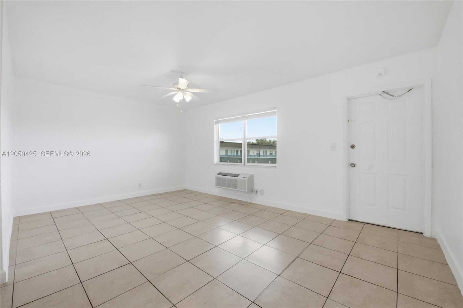 An empty room features white walls, tan tile flooring, a ceiling fan, and a window unit — MIRAMAR, FL