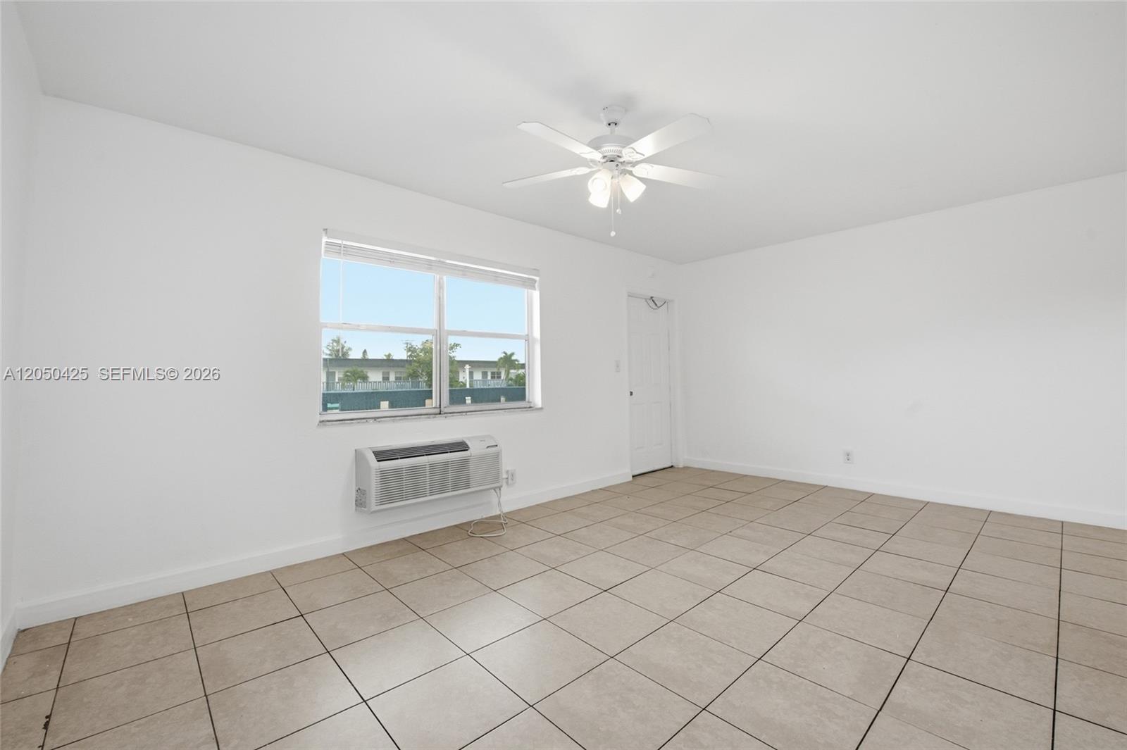 An empty room features white walls, beige tile flooring, a ceiling fan, and a window unit — MIRAMAR, FL