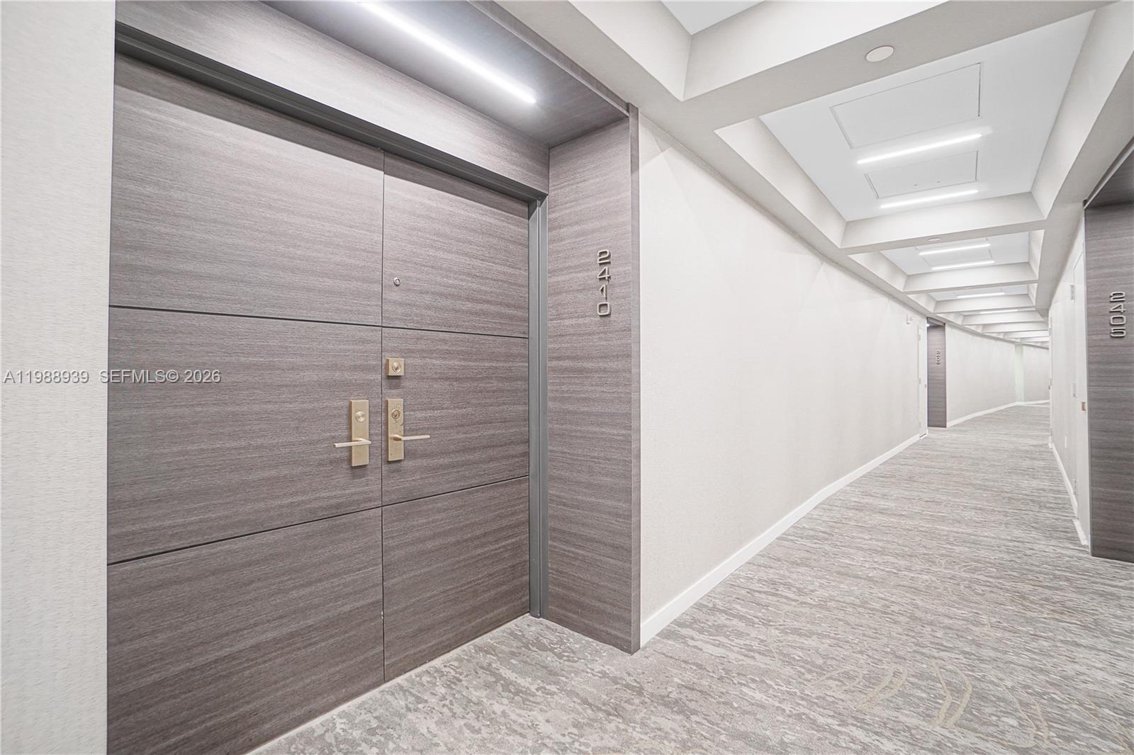 A modern apartment hallway features a wood-paneled door labeled 2410 and recessed ceiling lighting — 9 Island Ave # 2410, Miami Beach FL 33139, MIAMI BEACH, FL