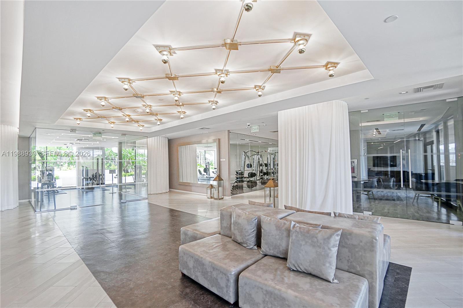 A modern lobby features a geometric ceiling light fixture, glass-walled gym, and modular gray seating — 9 Island Ave # 2410, Miami Beach FL 33139, MIAMI BEACH, FL