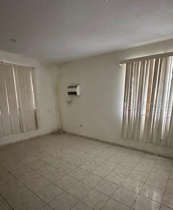 An empty room features light-colored tile flooring, two windows with vertical blinds, and a wall-mounted air conditioner — Carr. 635 Lote 1 BO. AIBONITO, HATILLO, PR