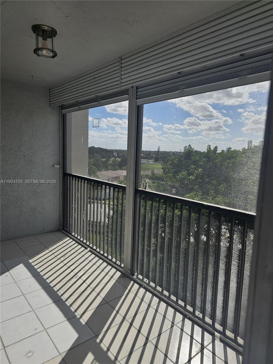 A balcony features white tile flooring, a black metal railing, and a view of trees — 3910 Inverrary Blvd # B, Lauderhill FL 33319, LAUDERHILL, FL