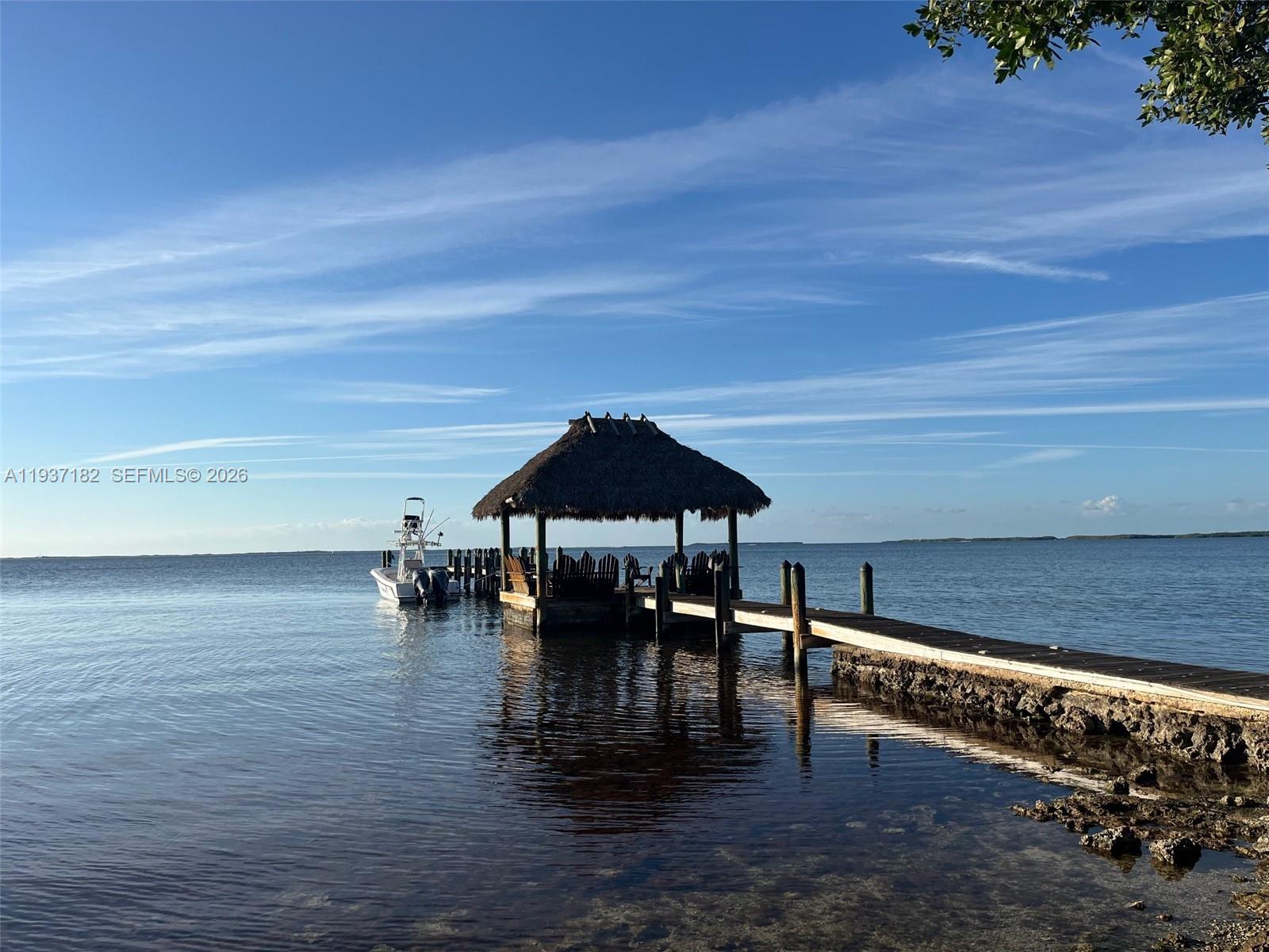 A wooden dock with a thatched-roof gazebo extends into the calm ocean water — 202 Sanctuary Dr, Key Largo FL 33037, KEY LARGO, FL