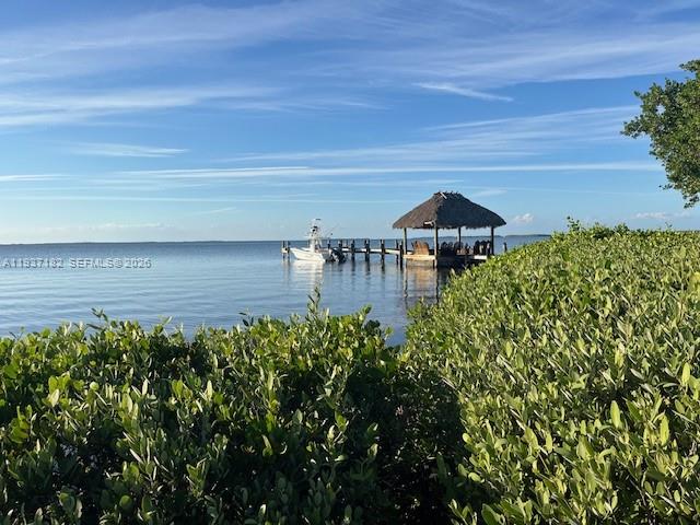 A boat is docked at a wooden pier with a thatched-roof gazebo on the water — 202 Sanctuary Dr, Key Largo FL 33037, KEY LARGO, FL