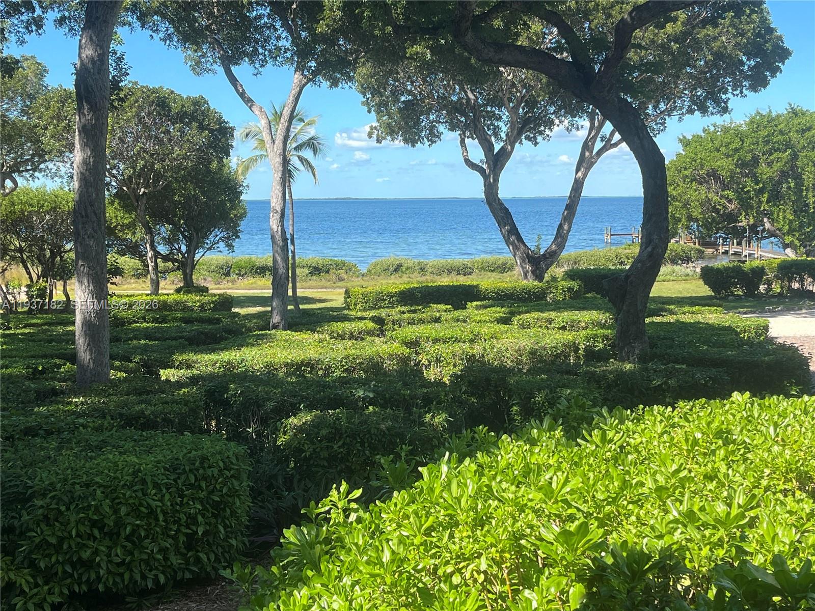 A view of a manicured hedge garden leading to a blue ocean and trees — 202 Sanctuary Dr, Key Largo FL 33037, KEY LARGO, FL