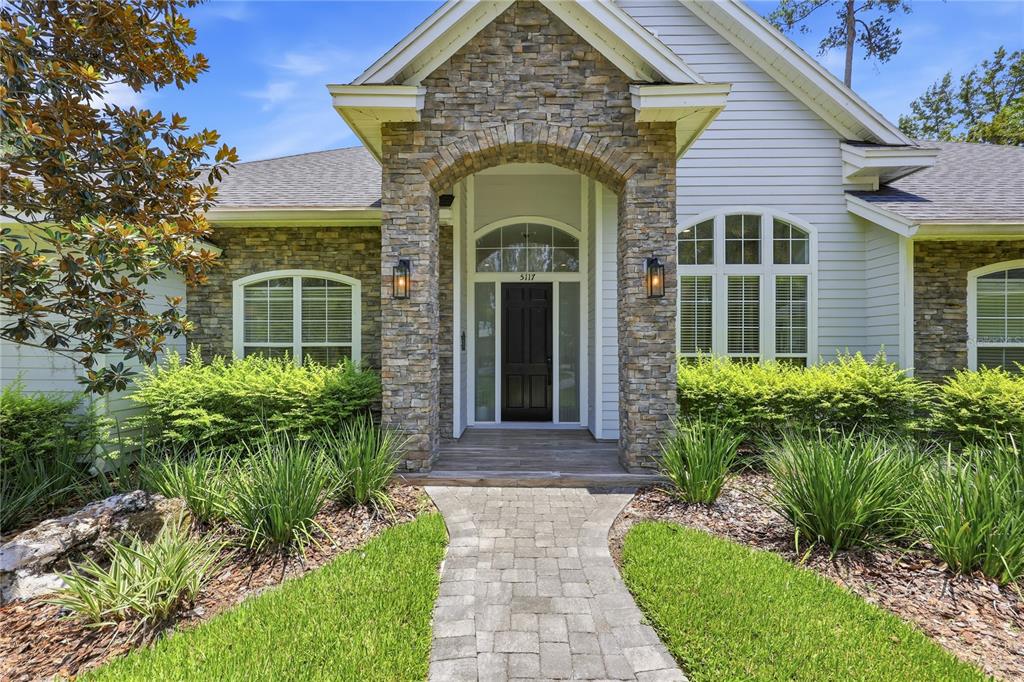 A stone-accented entryway with a black front door leads to a house with light siding — 5117 NW 55TH STREET, GAINESVILLE, FL