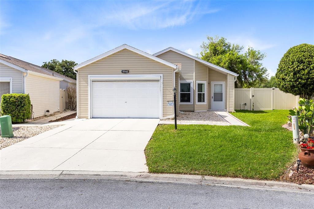 A beige single-story house features a white garage door, a front lawn, and a driveway — 4960 HERON RUN CIRCLE, LEESBURG, FL