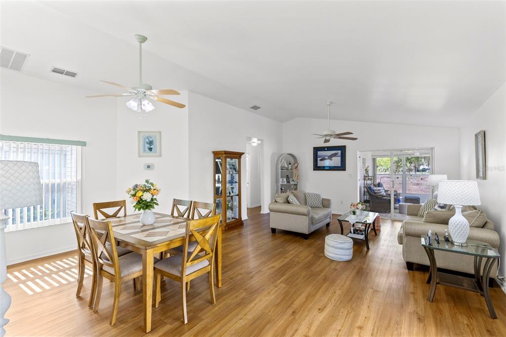 A dining and living area with wood-look flooring, vaulted ceilings, and two ceiling fans — 4960 HERON RUN CIRCLE, LEESBURG, FL